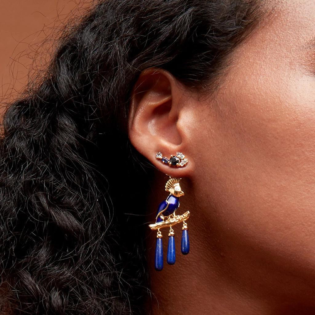 Model wearing a blue gemstone cluster ear climber with bold blue bird statement dangle attached below.