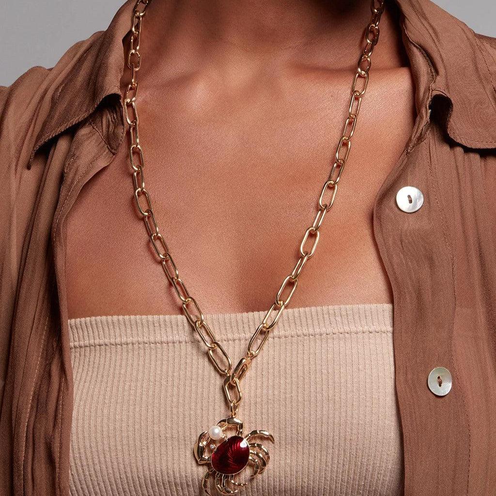 Gold paperclip necklace with red crab charm worn over a neutral outfit