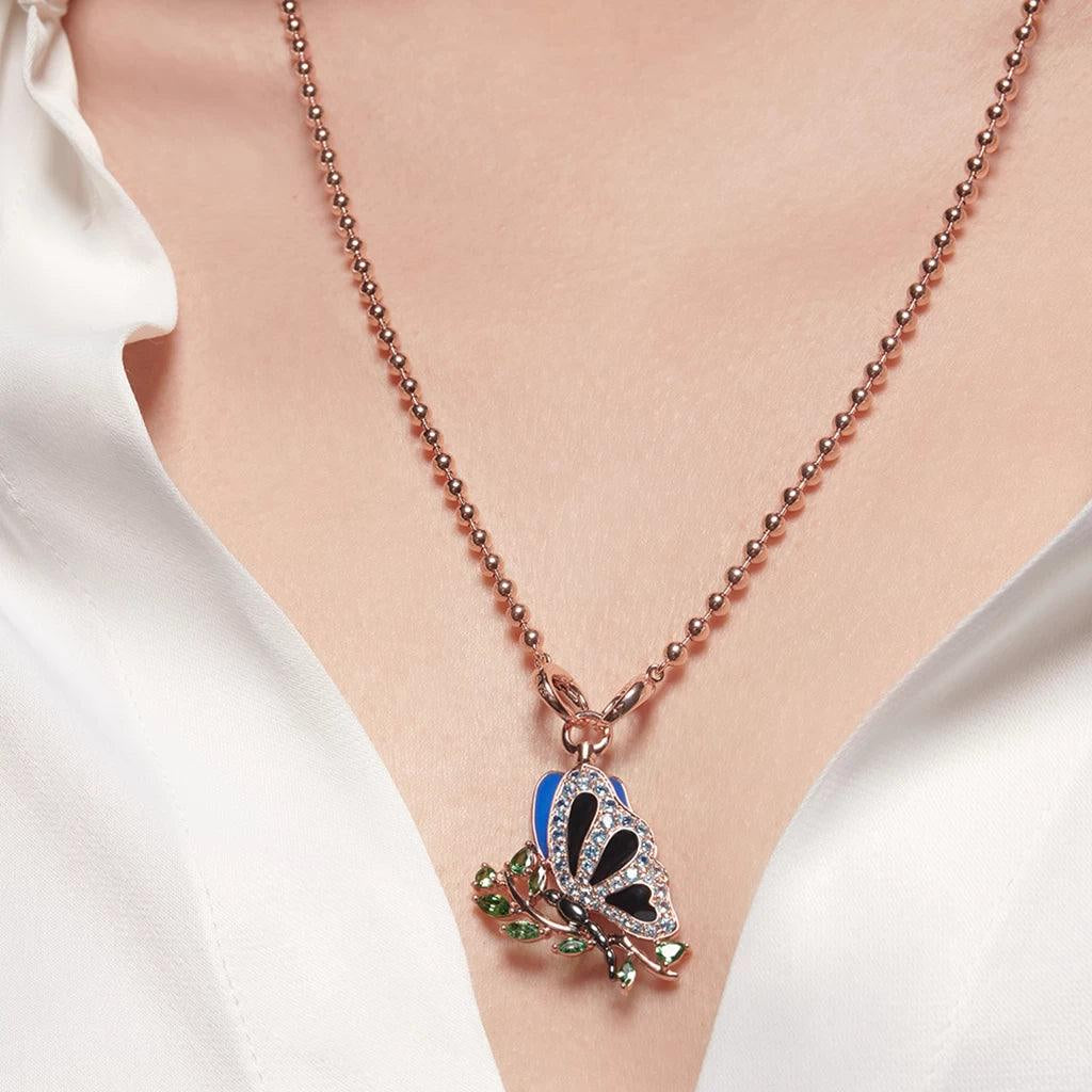 Rose gold ball chain necklace with enamel butterfly and green gemstone leaf charm on white blouse