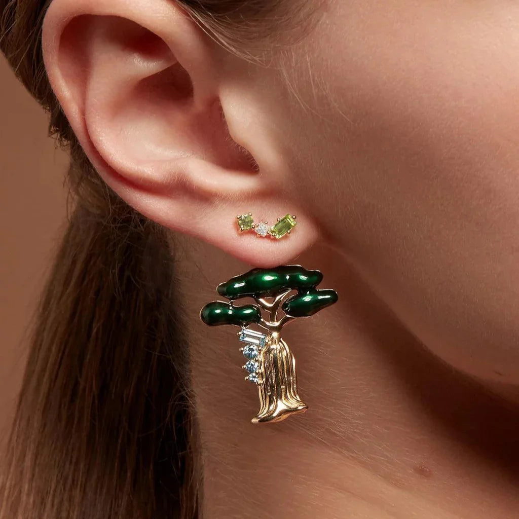 Close-up of ear with green peridot and diamond cluster studs paired with large green and gold tree charm.