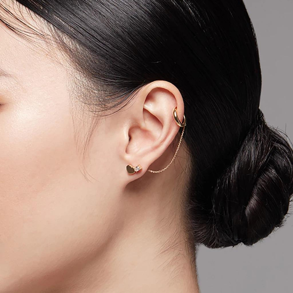 Gold-tone ear cuff with fine chain styled with heart-shaped stud on woman's ear