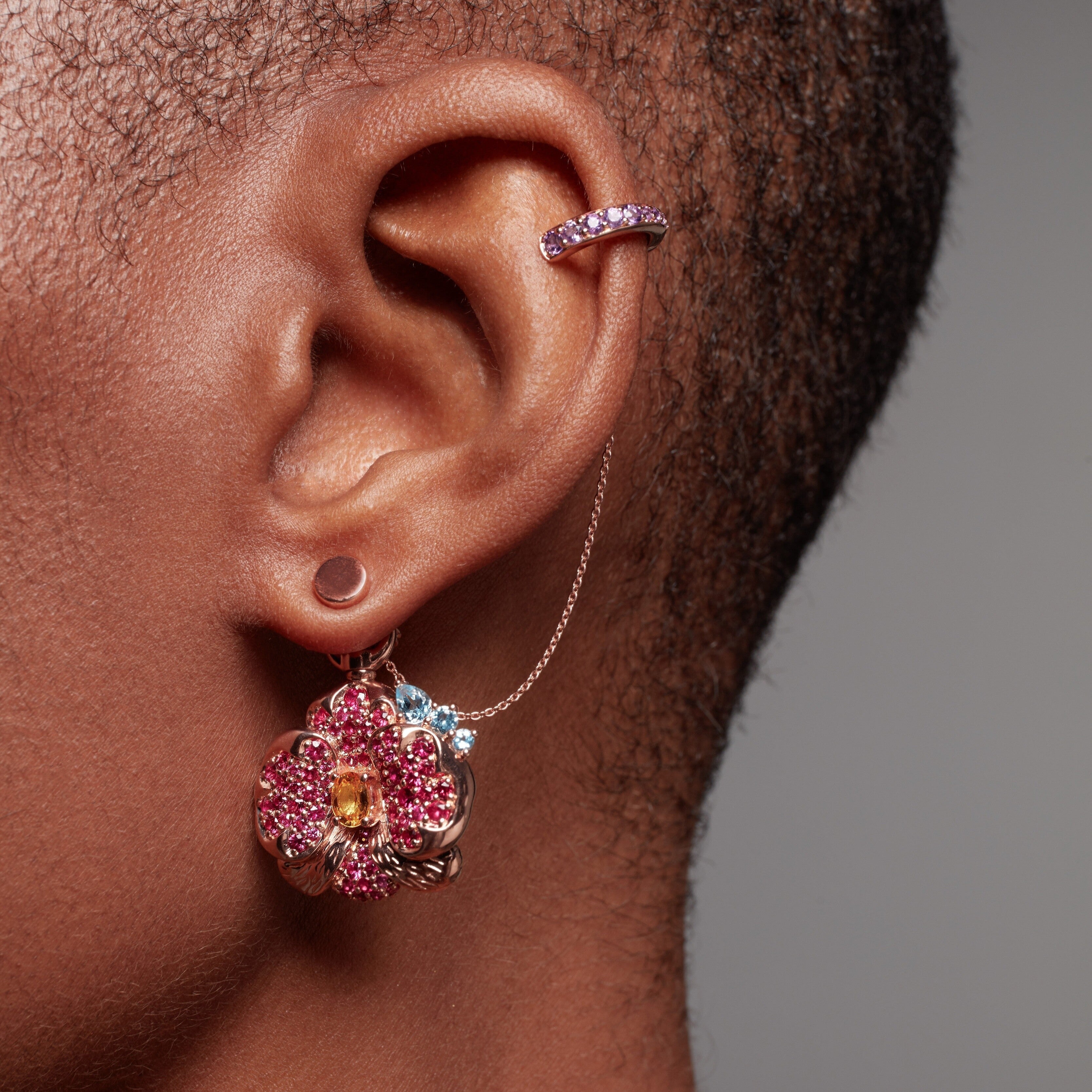 Close-up of ear with rose gold ear cuff and dangling pink flower charm earring.