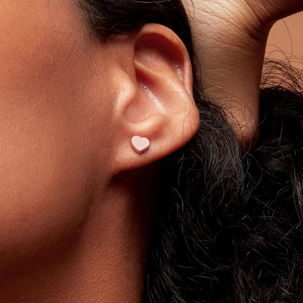 Close-up of an ear wearing a delicate light rose gold heart-shaped stud earring on the earlobe.