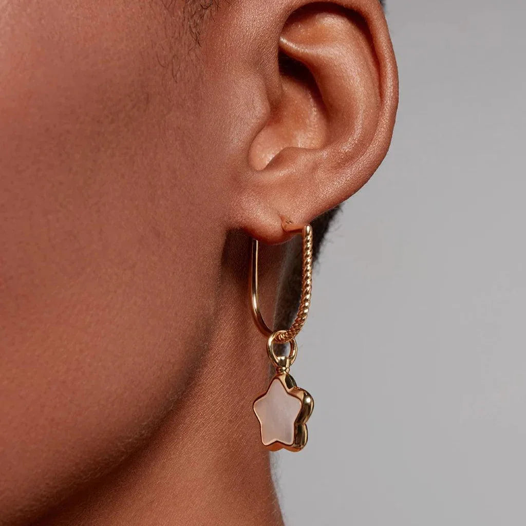 Close-up of an ear wearing a gold hoop earring with a dangling star-shaped charm inlaid with pearly white enamel.