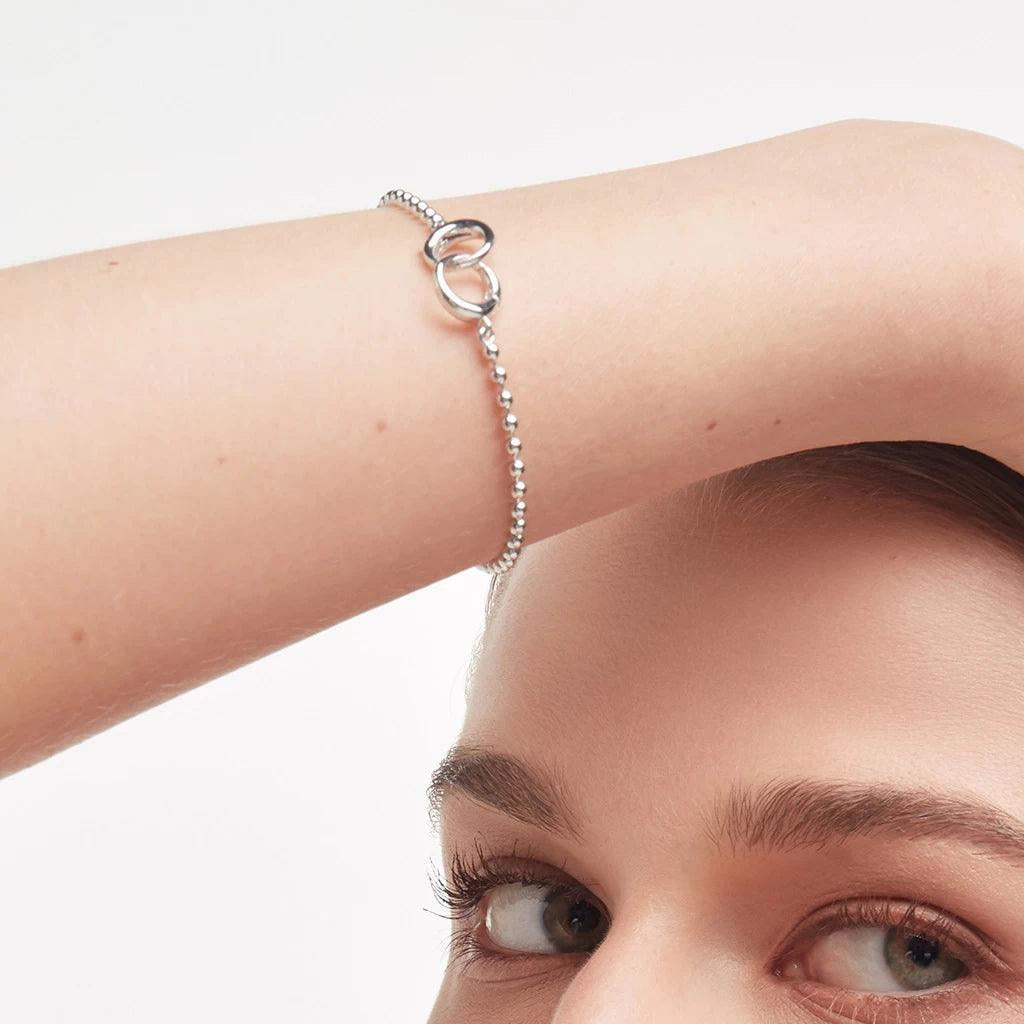 Silver beaded bracelet styled with interlocking loop clasp on model's wrist