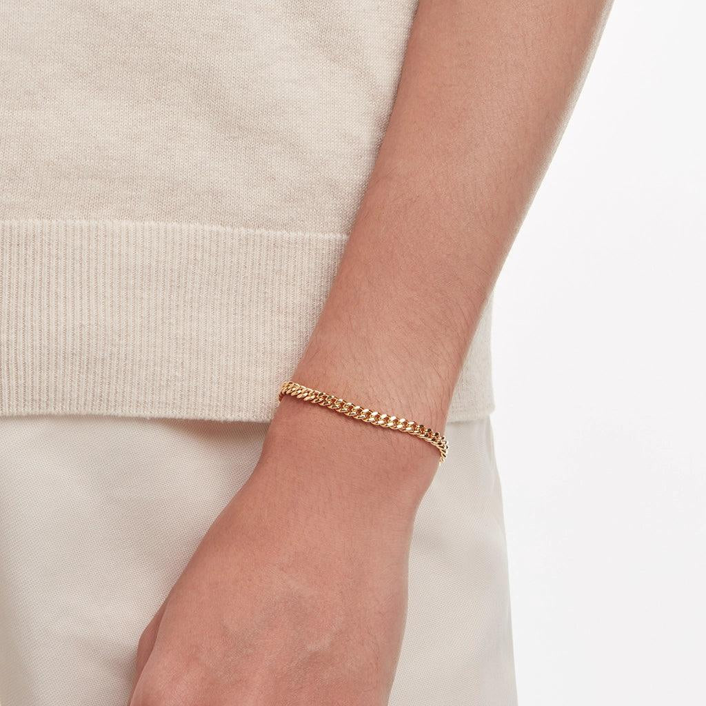 Men’s gold Cuban chain bracelet styled casually with neutral outfit.