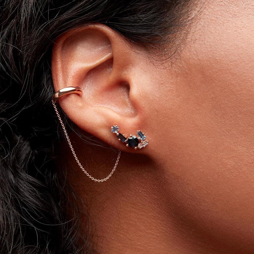 Close-up of ear with blue gemstone cluster ear climber connected to a rose gold chain cuff.