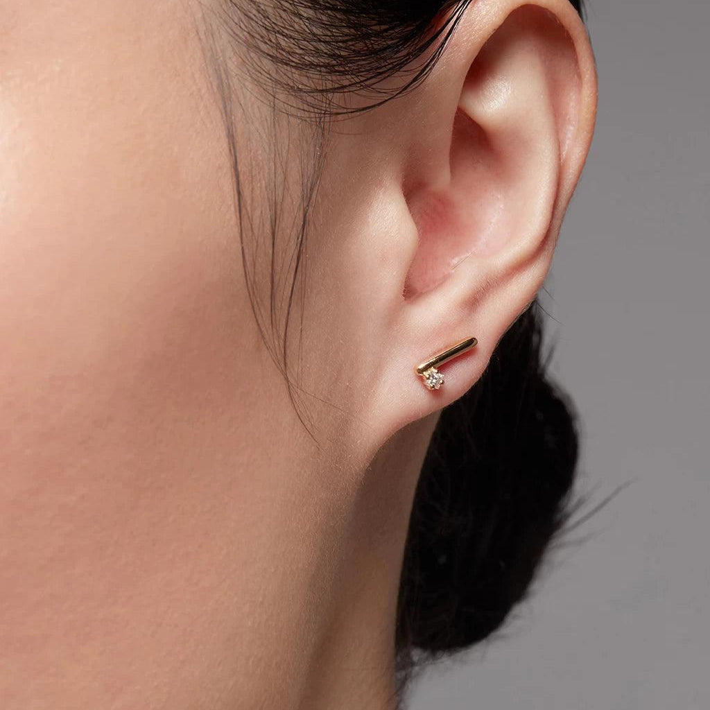 Yellow gold bar and diamond stud earring on ear close-up