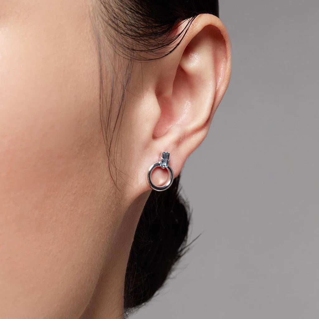 Silver hoop stud earring with rectangular light blue gemstone on ear.