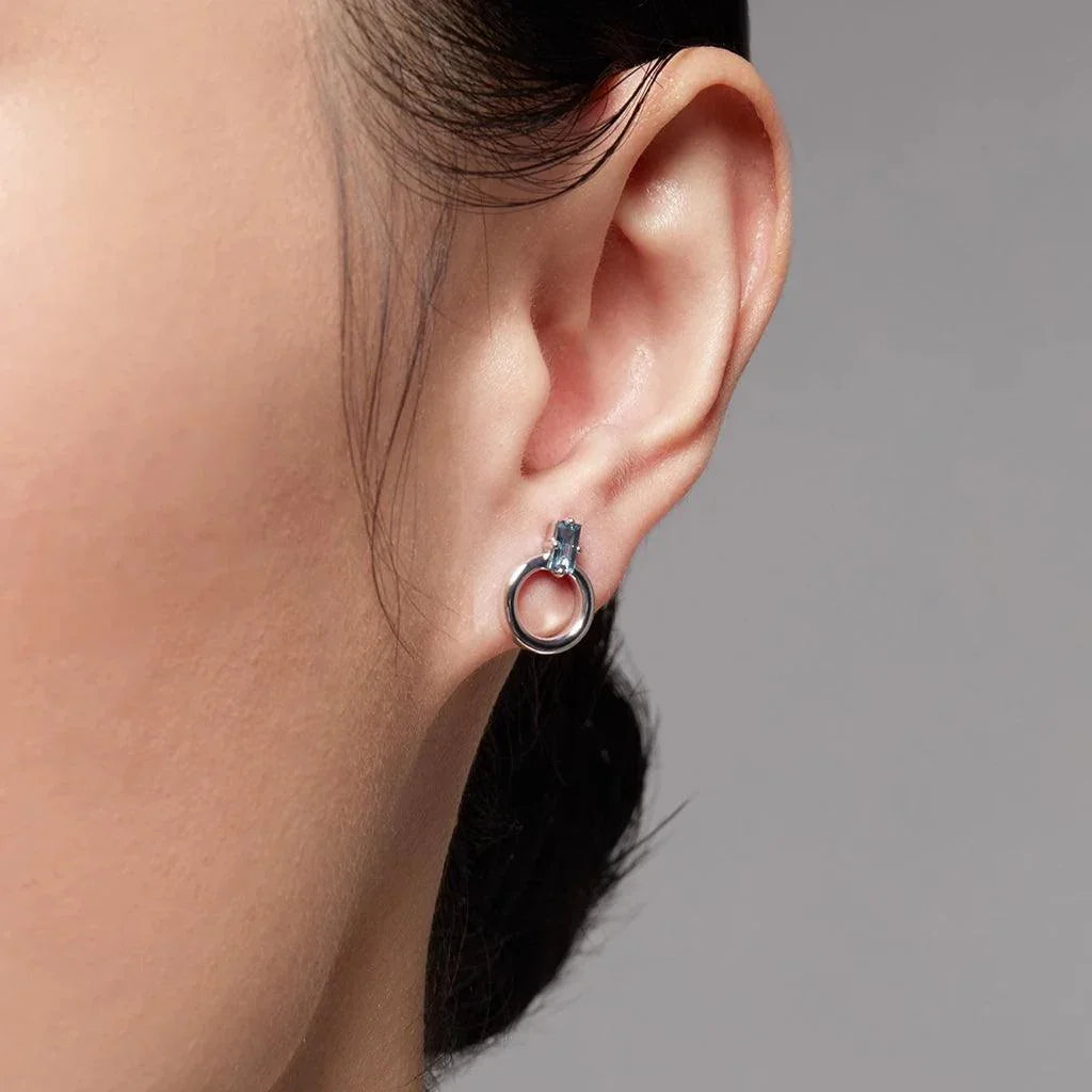 Silver hoop stud earring with rectangular light blue gemstone on ear.