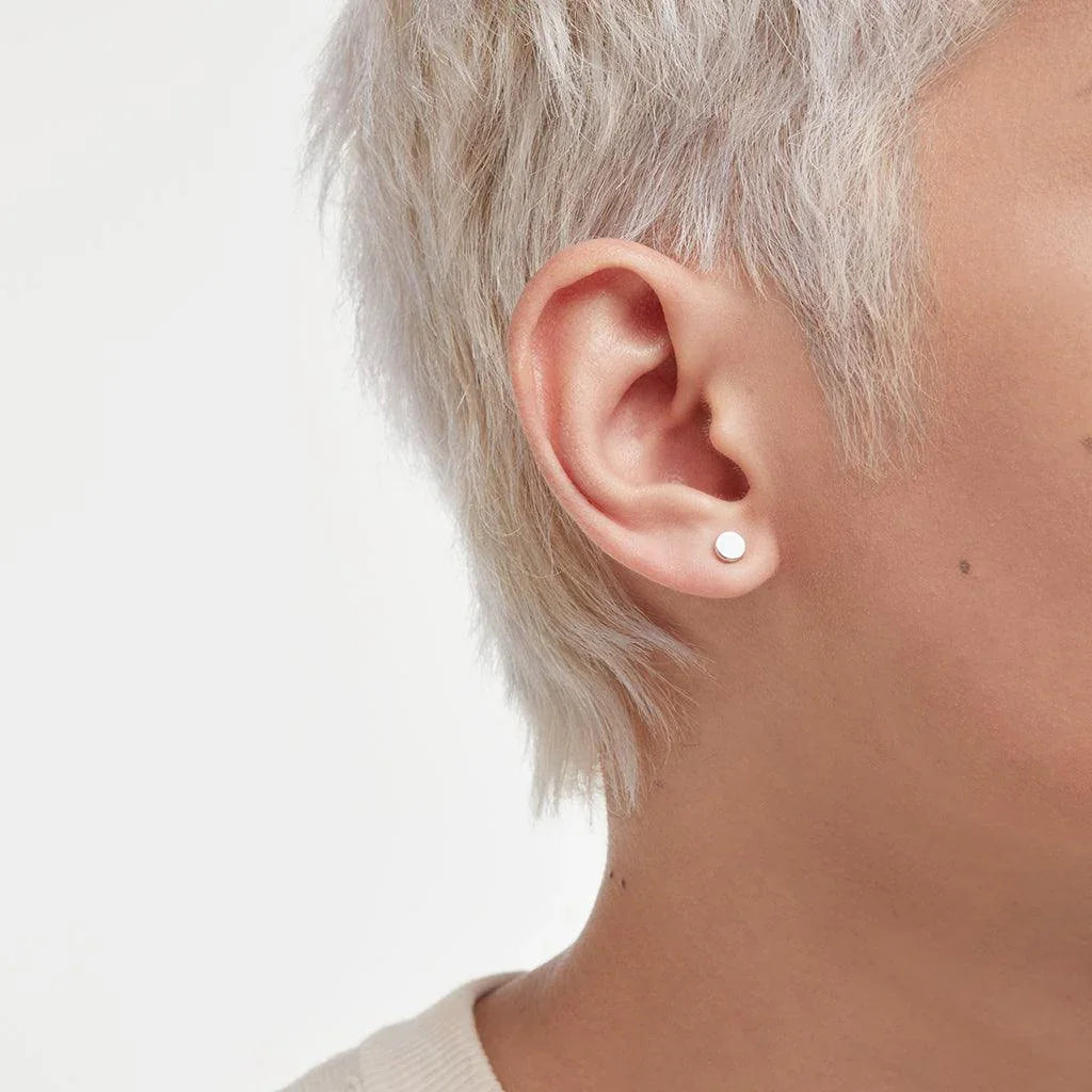 Side profile of a person with short, platinum blonde hair, wearing a small, round silver stud earring on the lobe for a minimalist look.