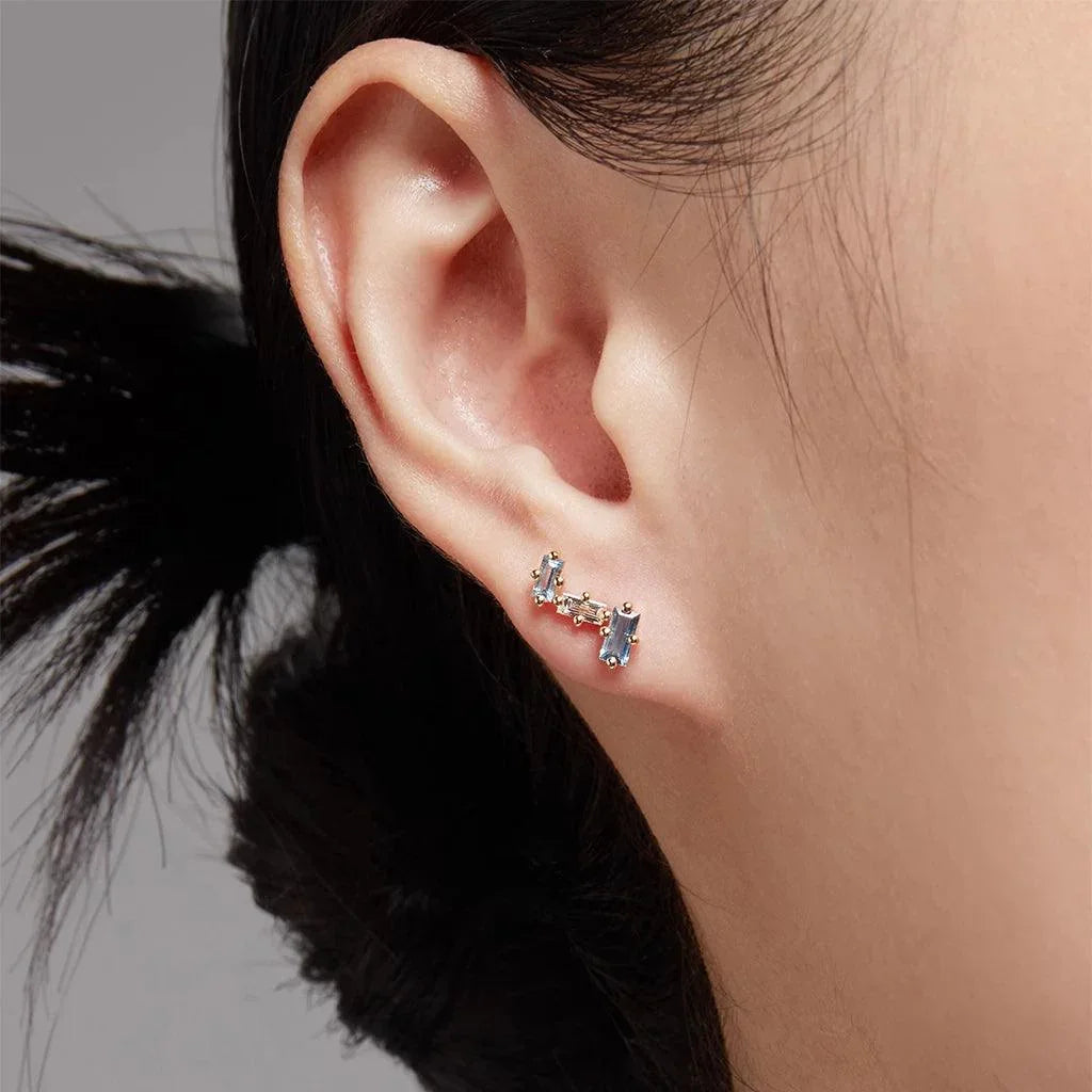 Close-up of ear wearing gold ear crawler with baguette-cut blue topaz stones.