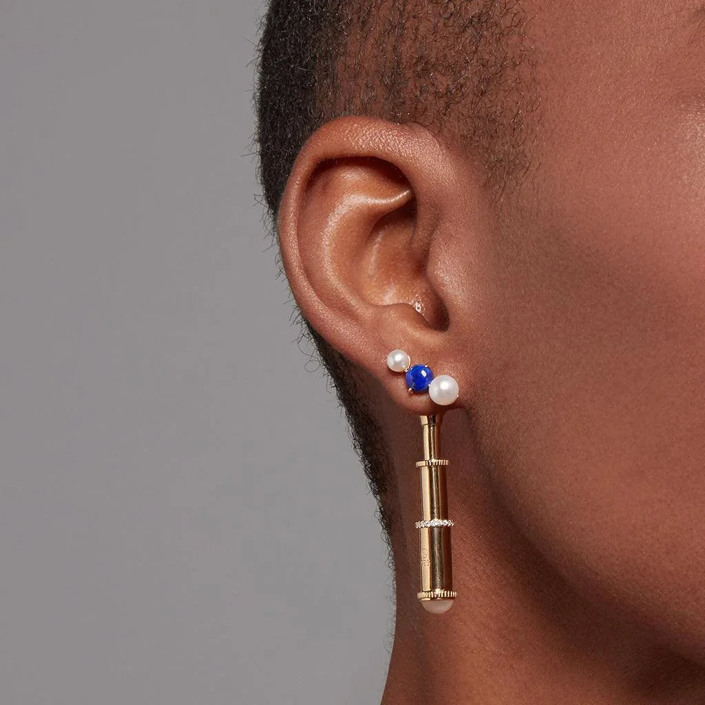 Ear wearing a three-stone pearl and lapis lazuli cluster stud with a detachable gold telescope charm.
