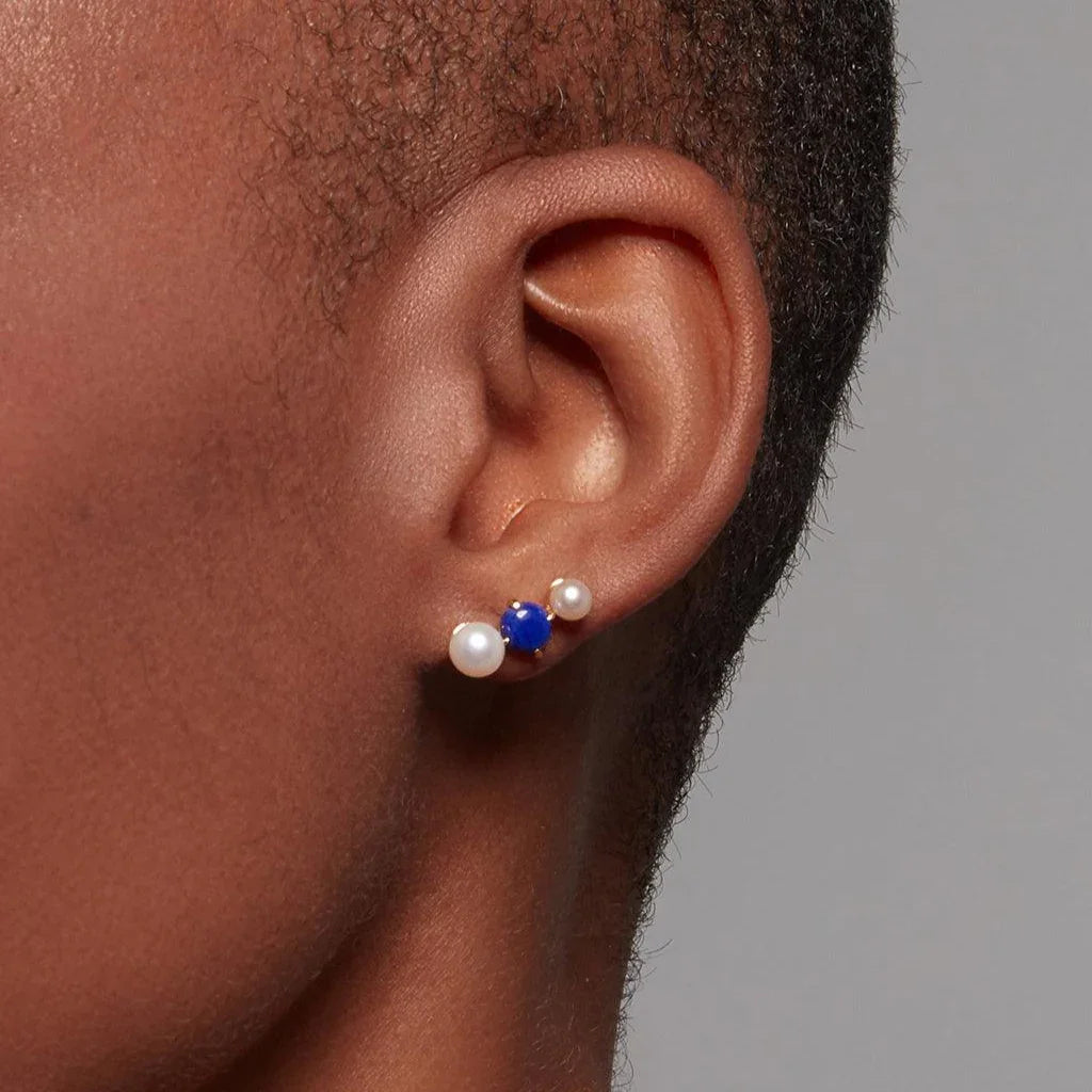 Close-up of simple pearl and lapis lazuli cluster stud earrings on ear.