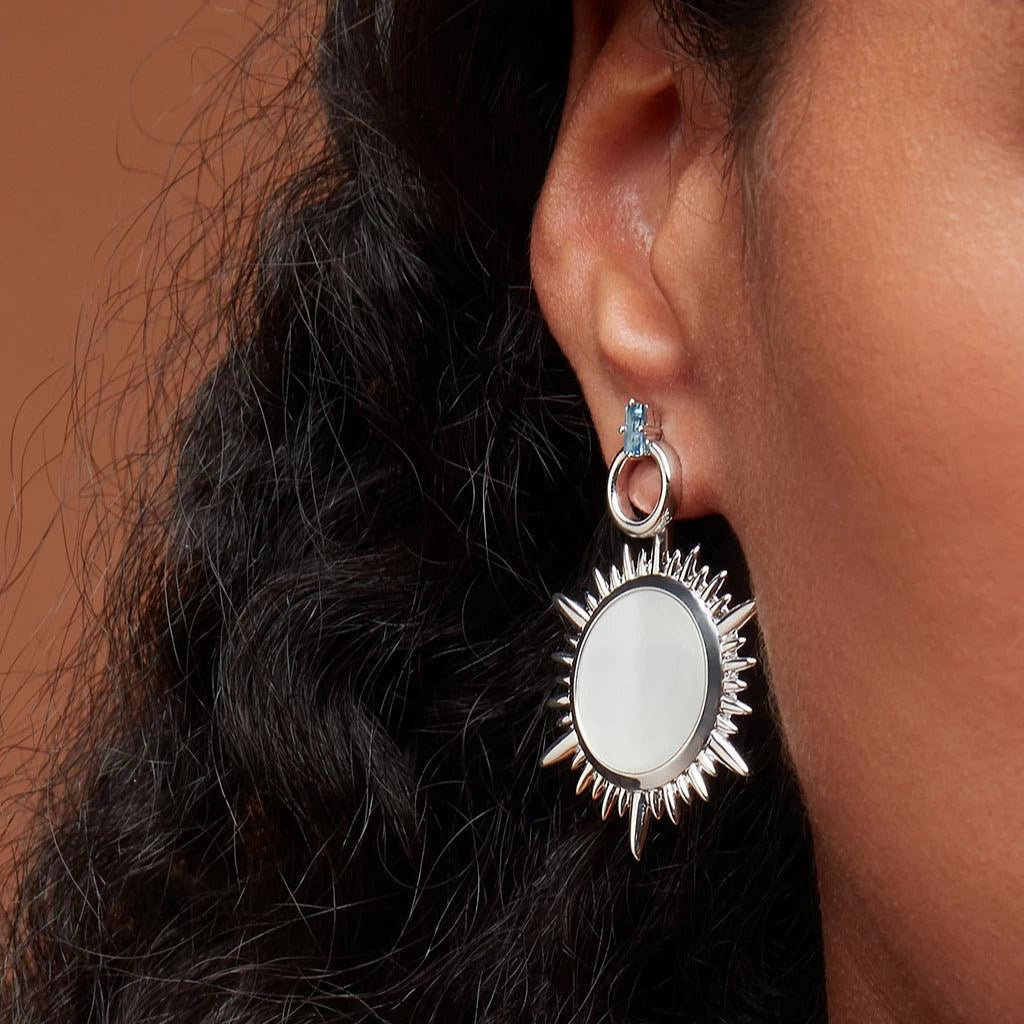 Hoop stud with blue gemstone worn with large sunburst charm.