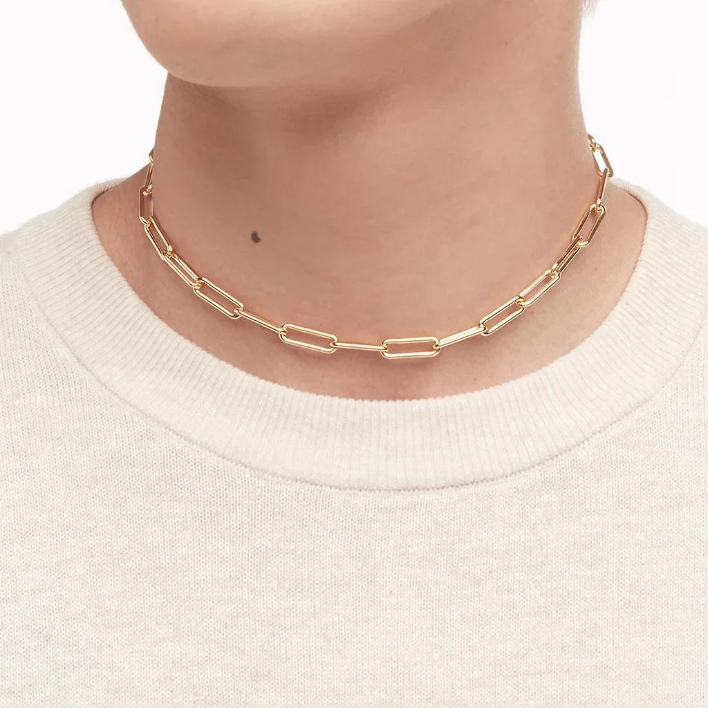 Gold paperclip chain choker worn with a neutral-toned sweater.