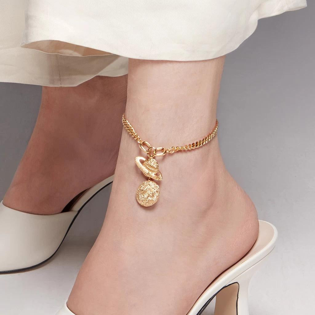 Celestial-themed gold anklet with planet and moon charms styled on ankle.
