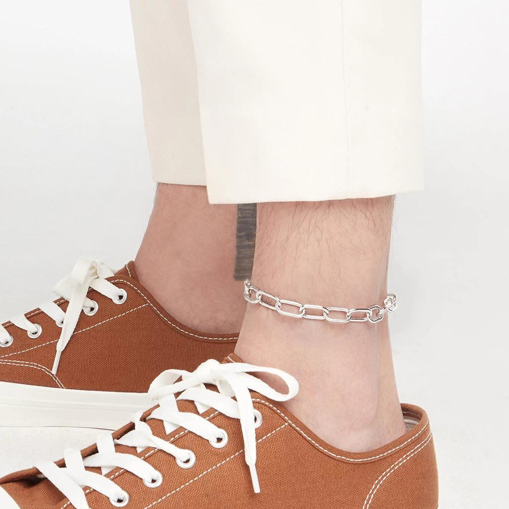 Minimalist silver link chain anklet worn by man with white pants and brown sneakers