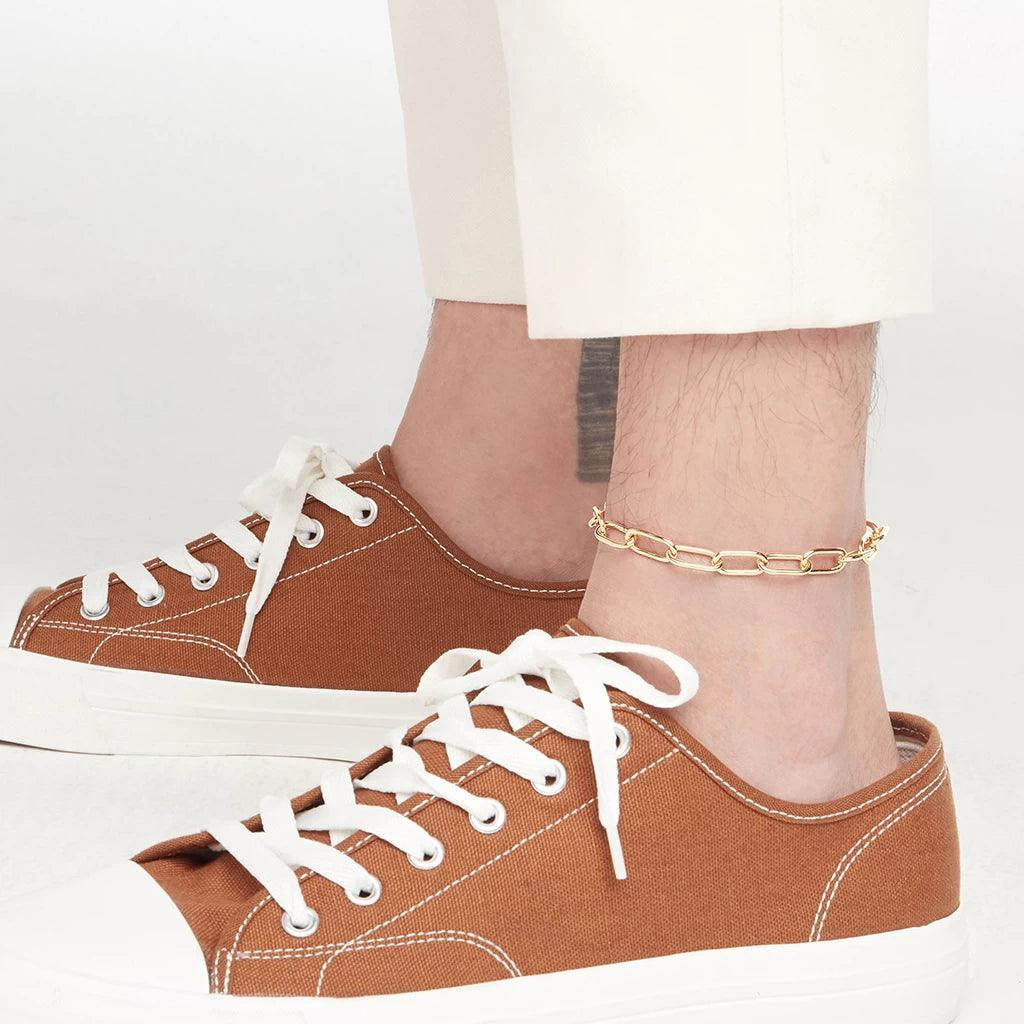 Gold paperclip link anklet styled on male ankle with casual white trousers and sneakers