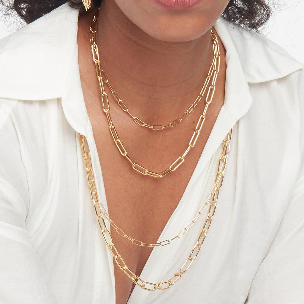 Close-up of woman layering three gold paperclip chain necklaces in different lengths.