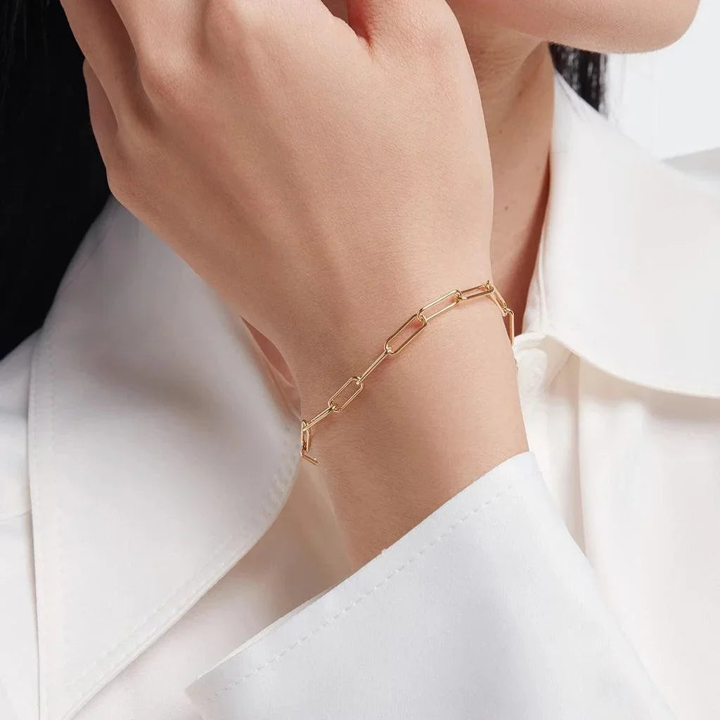 Gold chain link bracelet on wrist styled with white shirt – minimalist fine jewelry.