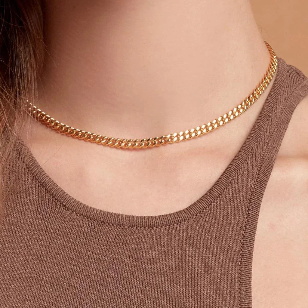 Close-up of a woman wearing a sleek gold Cuban link choker necklace with a brown tank top.