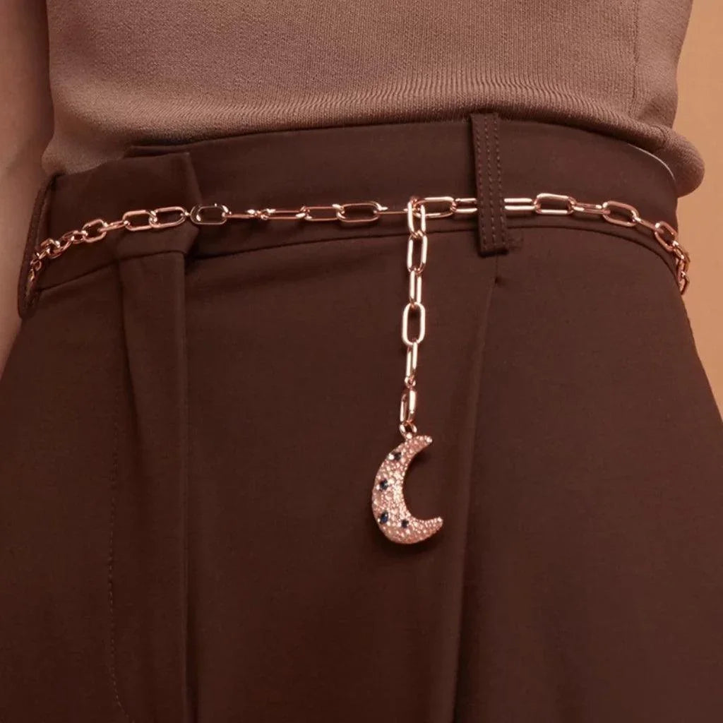 Rose gold chain belt with crescent moon charm styled on high-waisted trousers