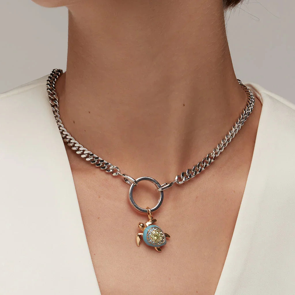 Close-up of a silver chain necklace with a gold and blue sea turtle charm pendant worn on a woman’s neck.