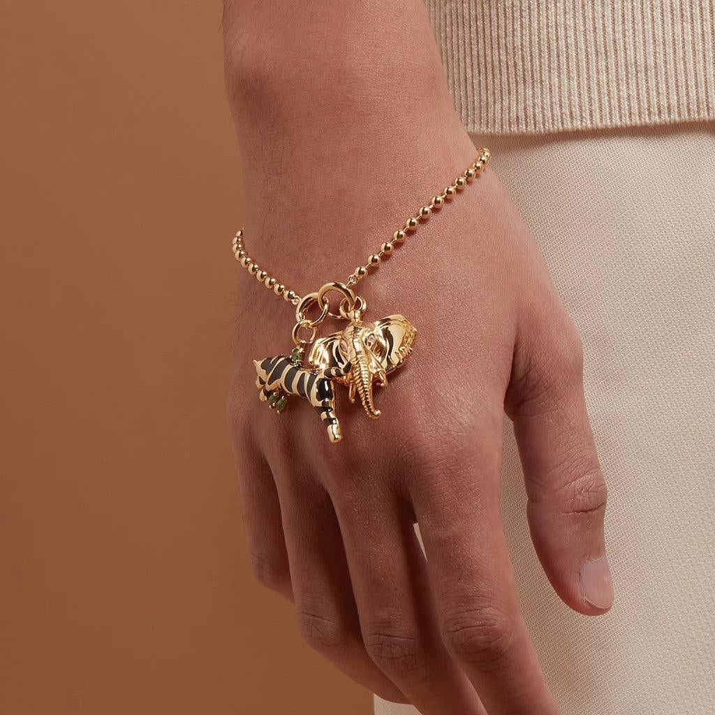 Gold charm bracelet with tiger and elephant charms on wrist