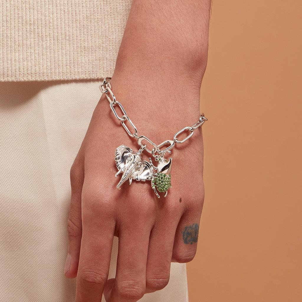 Silver charm bracelet featuring an elephant and green spiky beetle charm on wrist.
