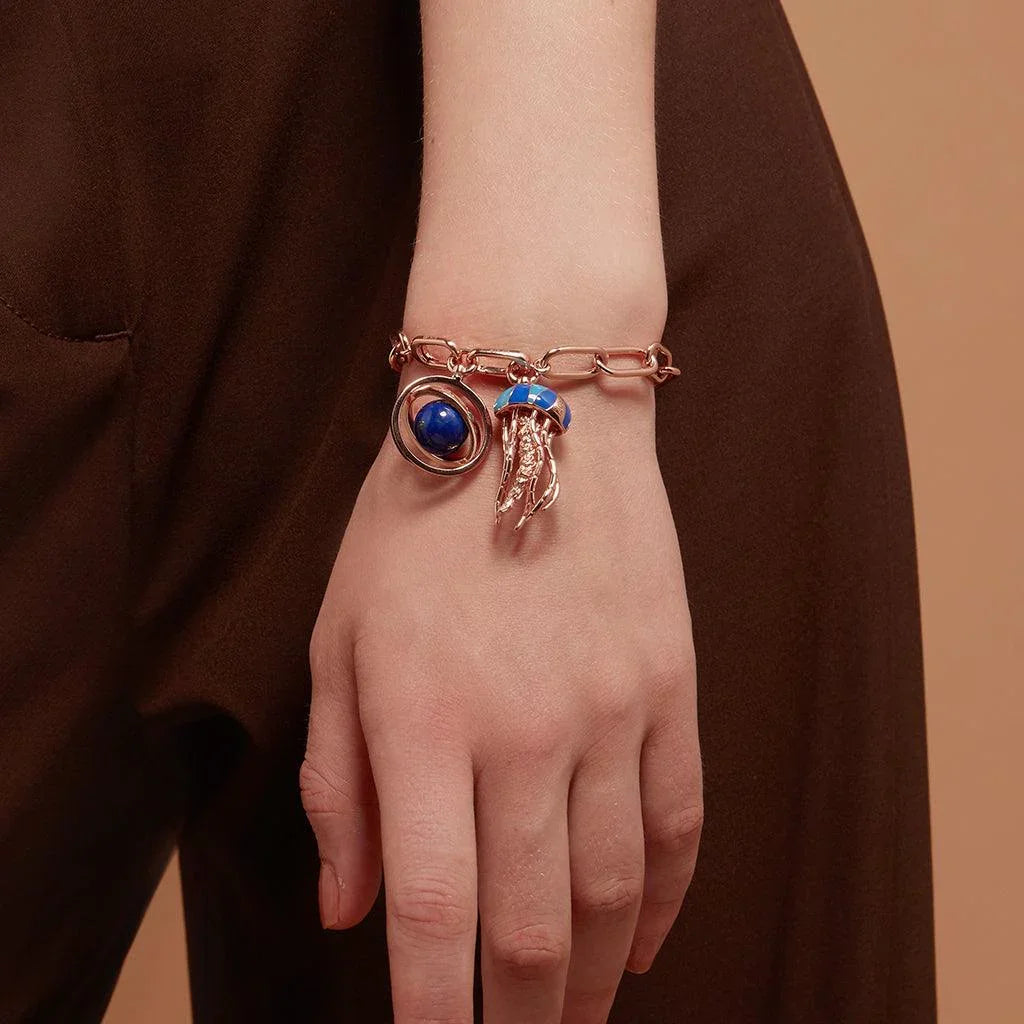 Rose gold charm bracelet with blue jellyfish and planetary charms on model's wrist.