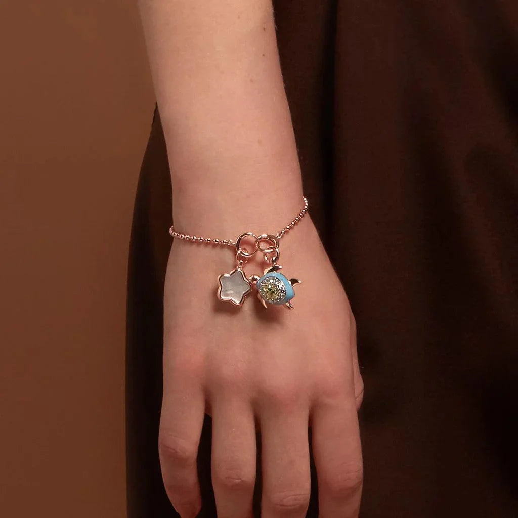 Rose gold bracelet with turtle and star charms on model’s wrist