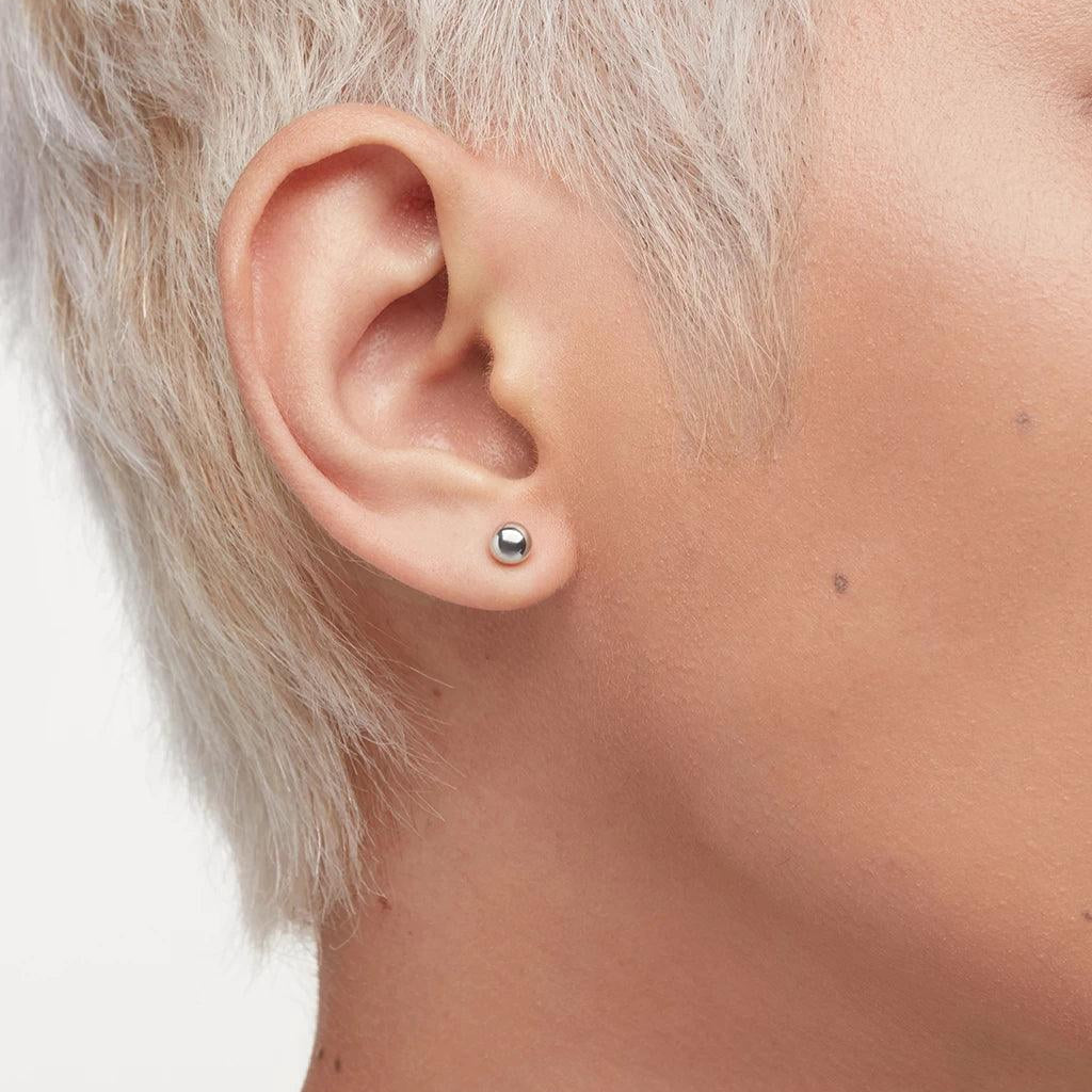 Close-up of a person's ear with a simple, small, round silver ball stud earring.