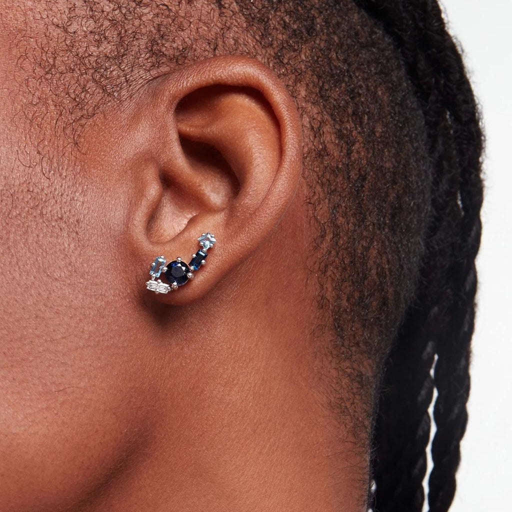 Close-up of ear wearing a blue gemstone cluster ear climber earring with light and dark blue stones in silver setting.