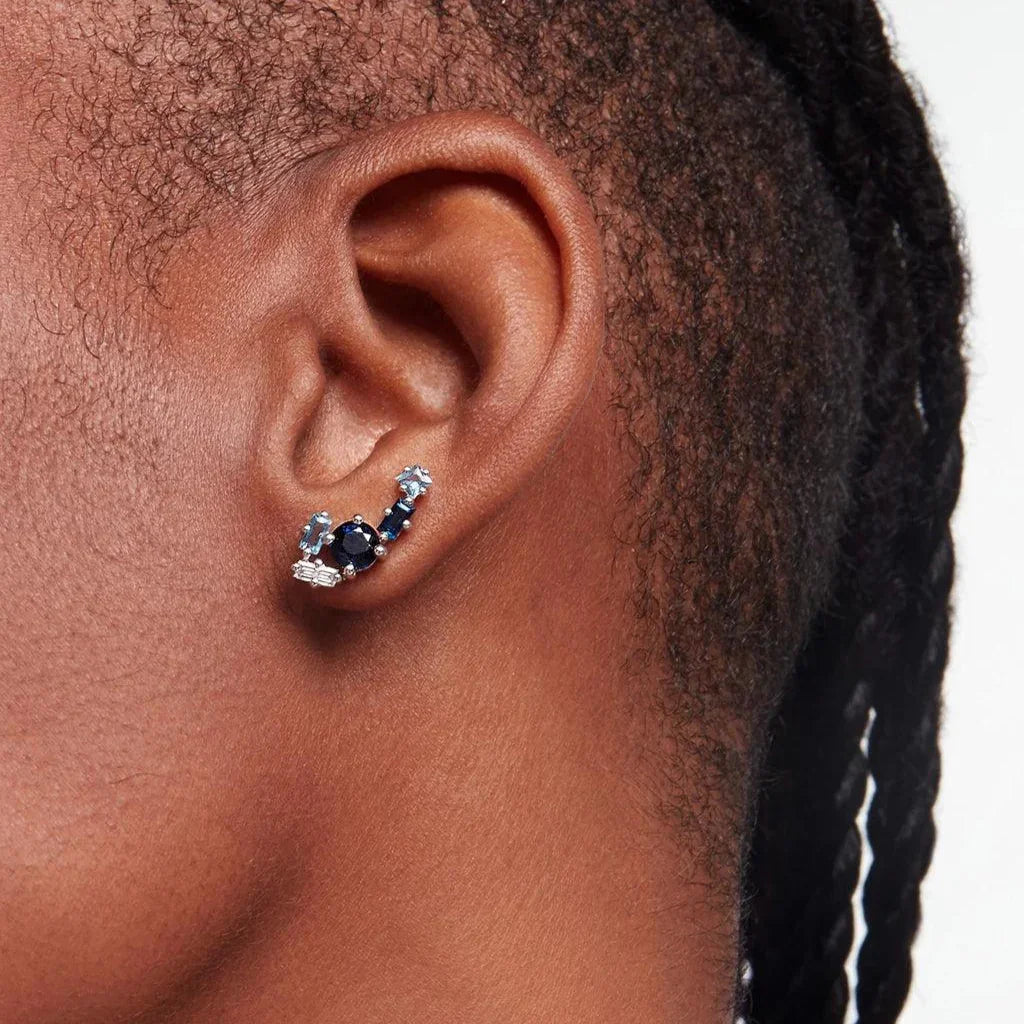 Close-up of ear wearing a blue gemstone cluster ear climber earring with light and dark blue stones in silver setting.