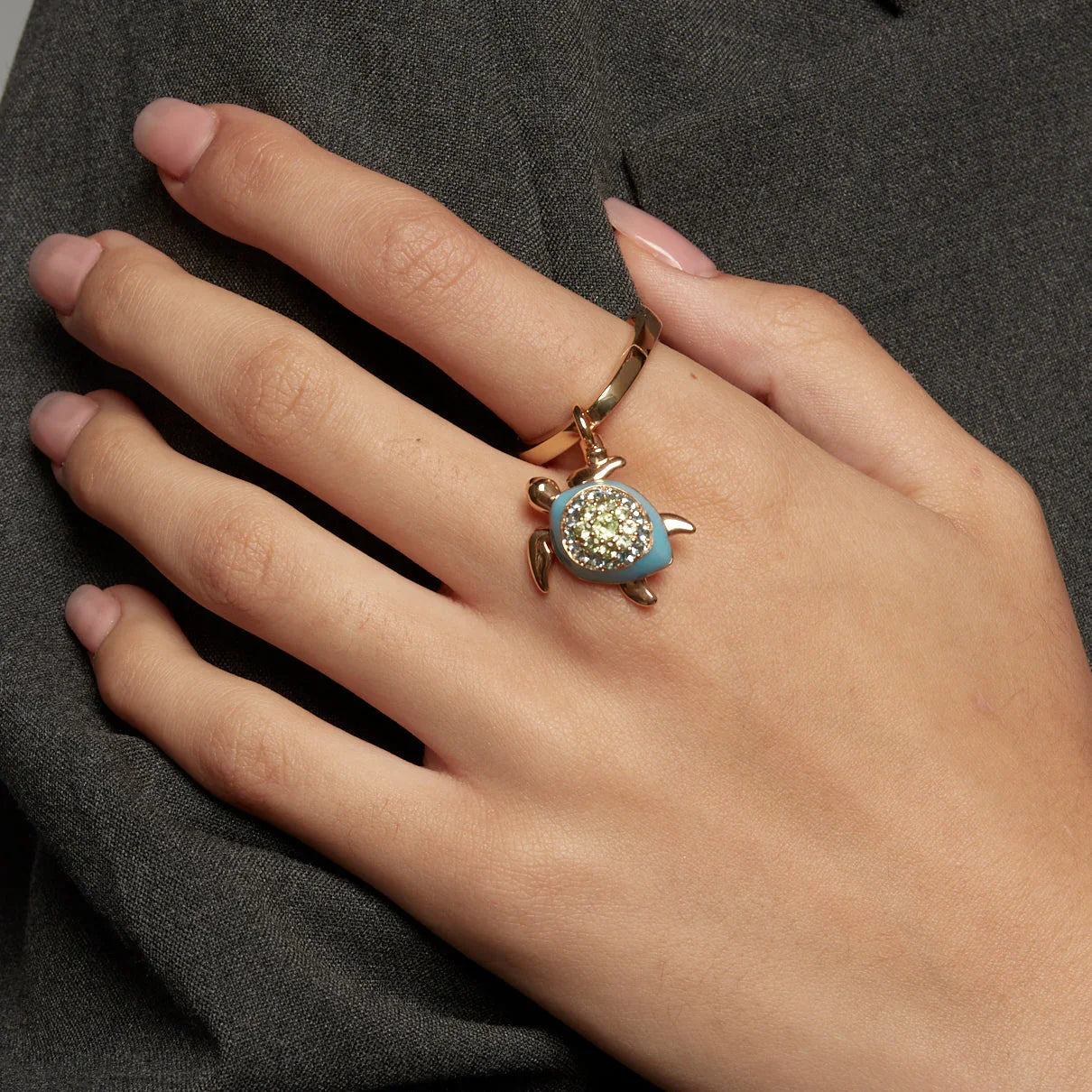 Gold ring featuring a sparkling turtle charm with a turquoise enamel shell, styled on a woman’s hand.