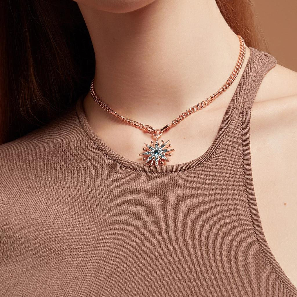 Woman wearing a rose gold choker necklace with a blue gemstone starburst charm styled with a brown tank top.