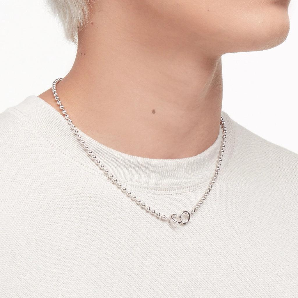 Close-up of silver beaded chain necklace on a person wearing a white sweater.