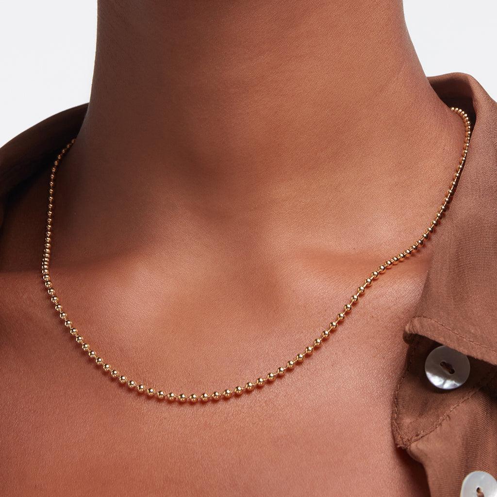 Close-up of a woman wearing a gold beaded chain necklace over a brown shirt