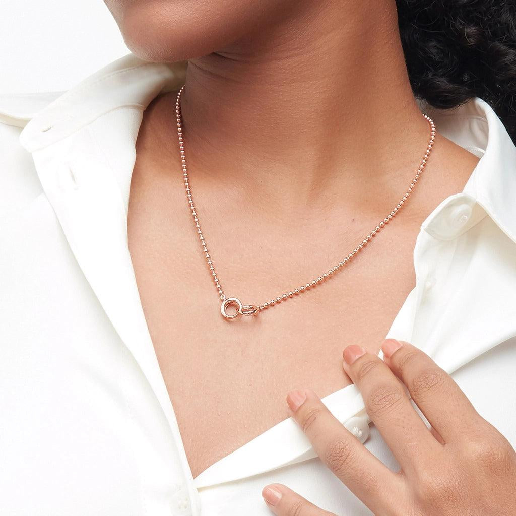Rose gold ball chain necklace with a round clasp worn with a white button-down shirt.