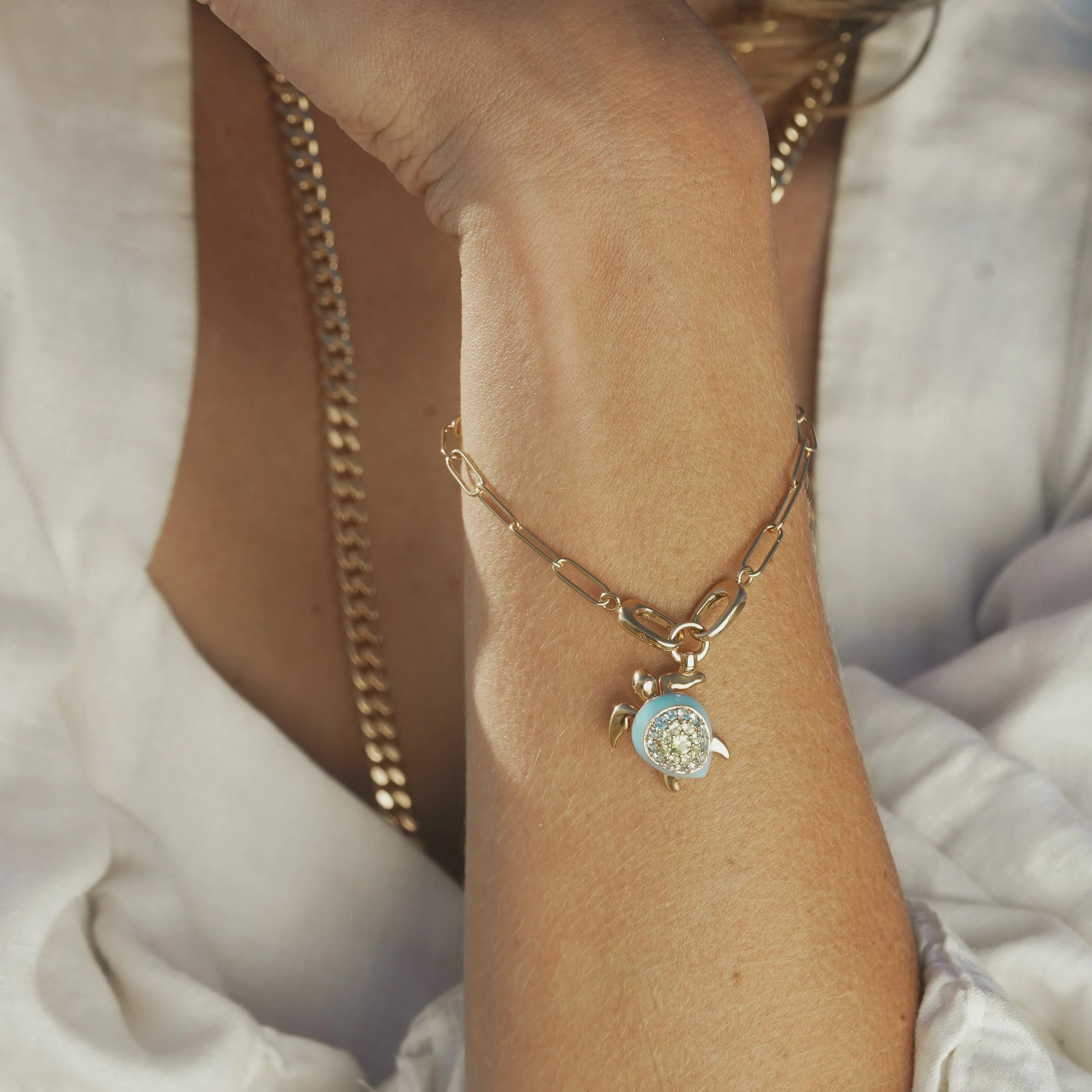 Delicate gold chain bracelet adorned with a glittering turtle charm with a blue enamel shell, worn on wrist.