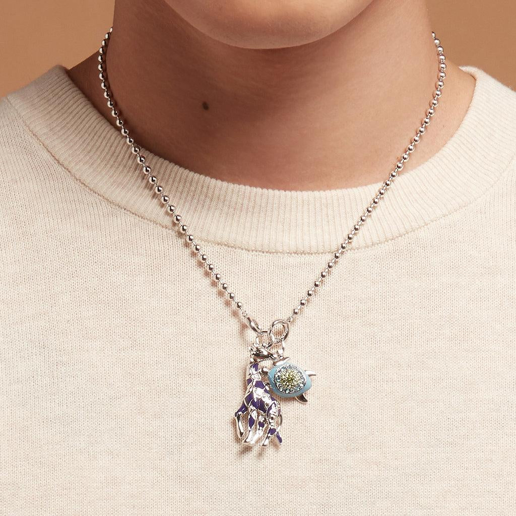 Silver beaded chain necklace styled with giraffe and turtle charms on a cream sweater
