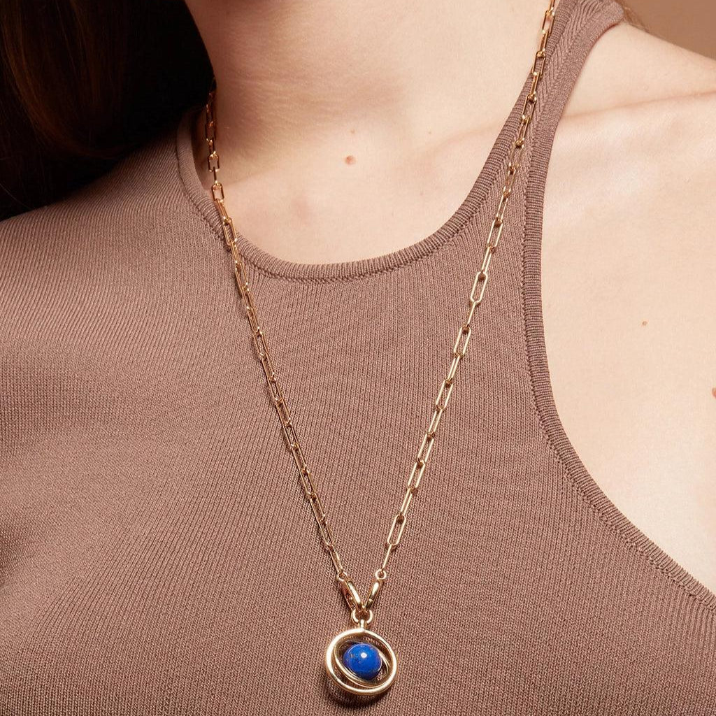 Gold paperclip chain necklace with a round cosmic blue orb pendant styled over a brown top.