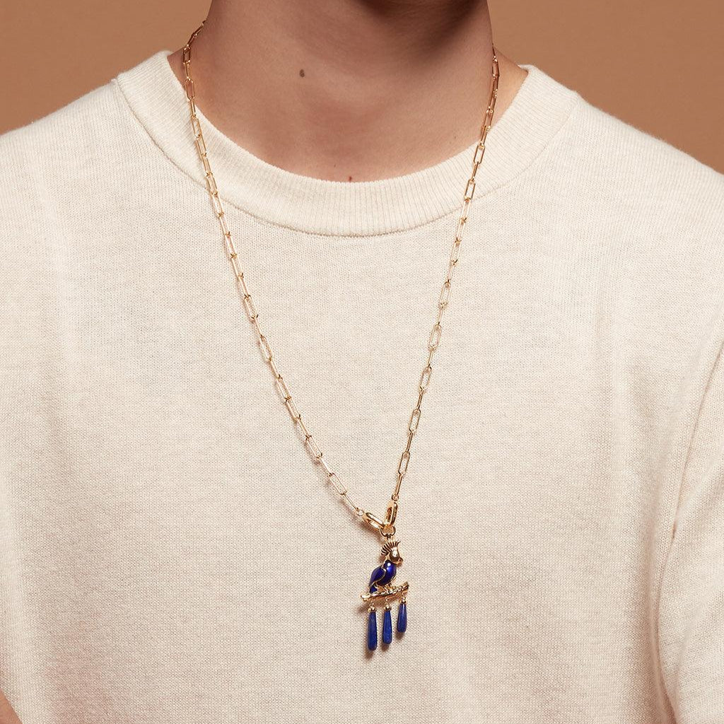 Model wearing gold paperclip chain necklace with blue bird charm pendant.