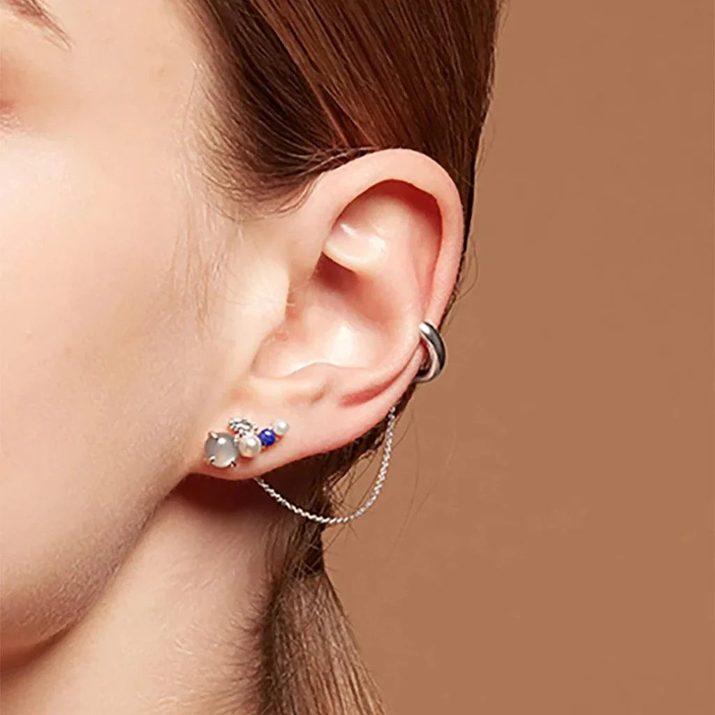 Silver-tone ear cuff with delicate chain paired with multiple gemstone studs on woman's ear
