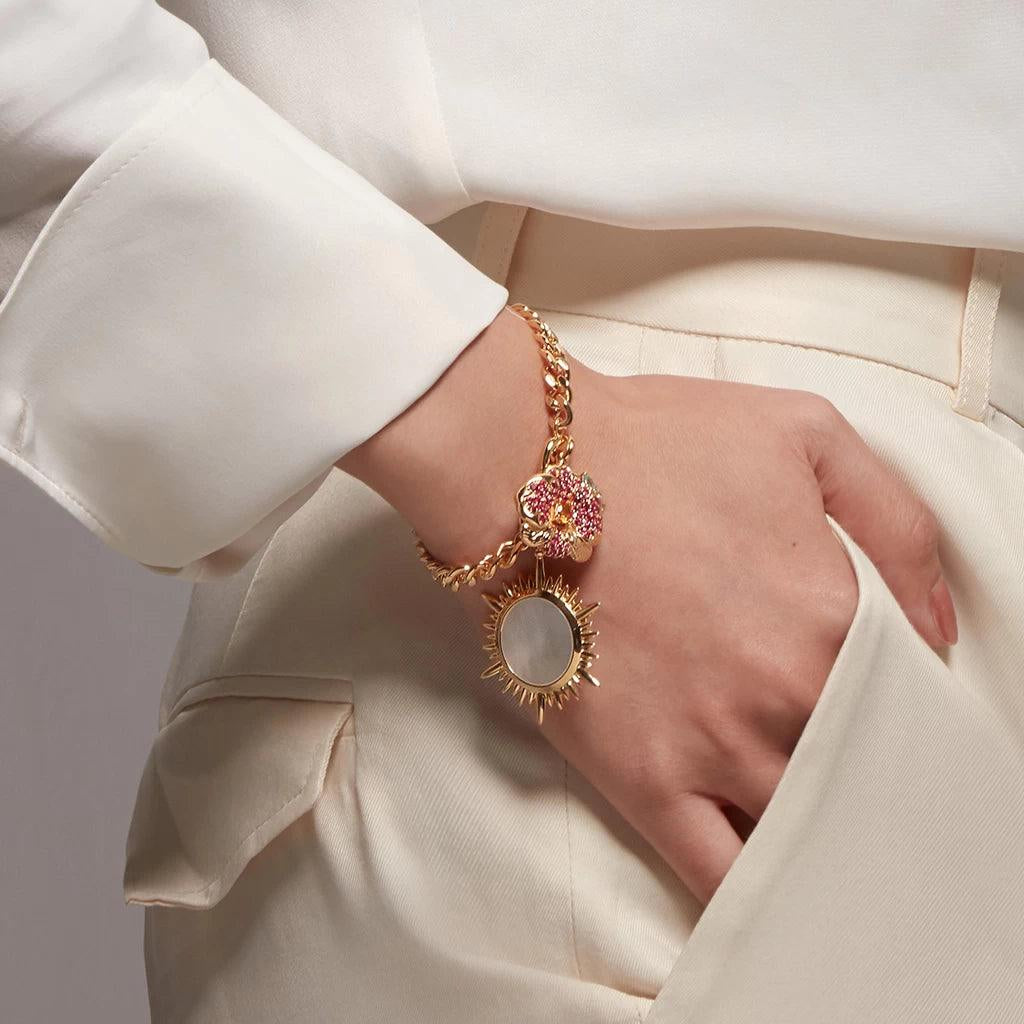 Gold chain bracelet with pink flower and mother-of-pearl sun charms on wrist