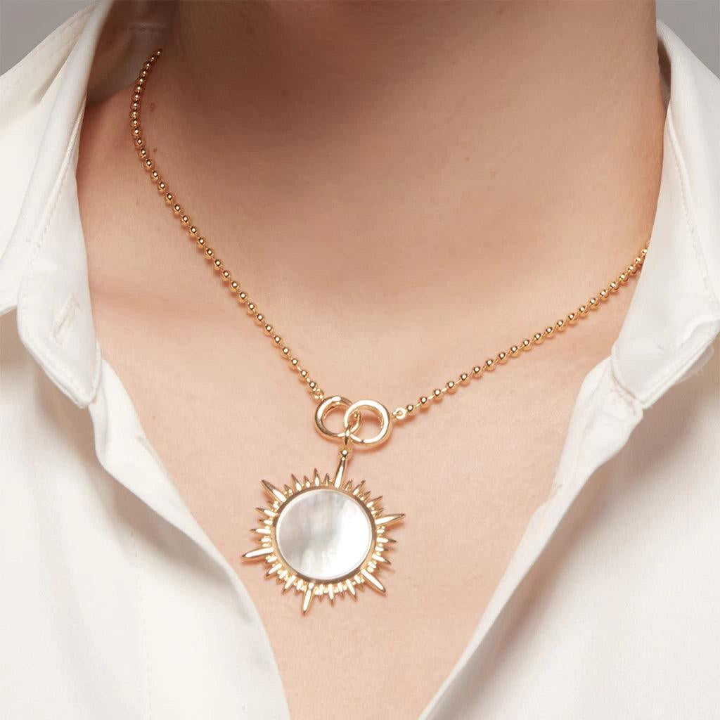 Gold ball chain necklace with a radiant sunburst charm featuring a white mother-of-pearl center