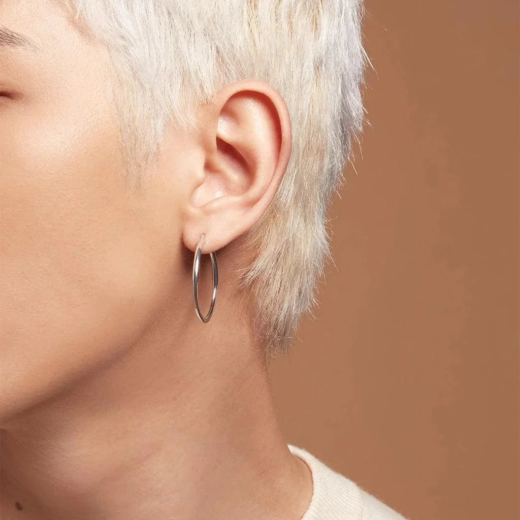 Close-up of a person's ear with platinum blonde hair, wearing a simple, classic polished silver round hoop earring.