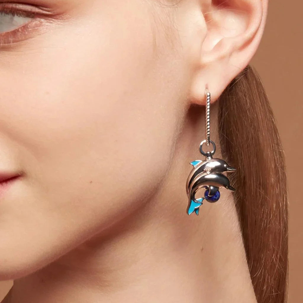 Close-up of silver dolphin charm earring with blue accents and lapis bead, worn on model's ear.