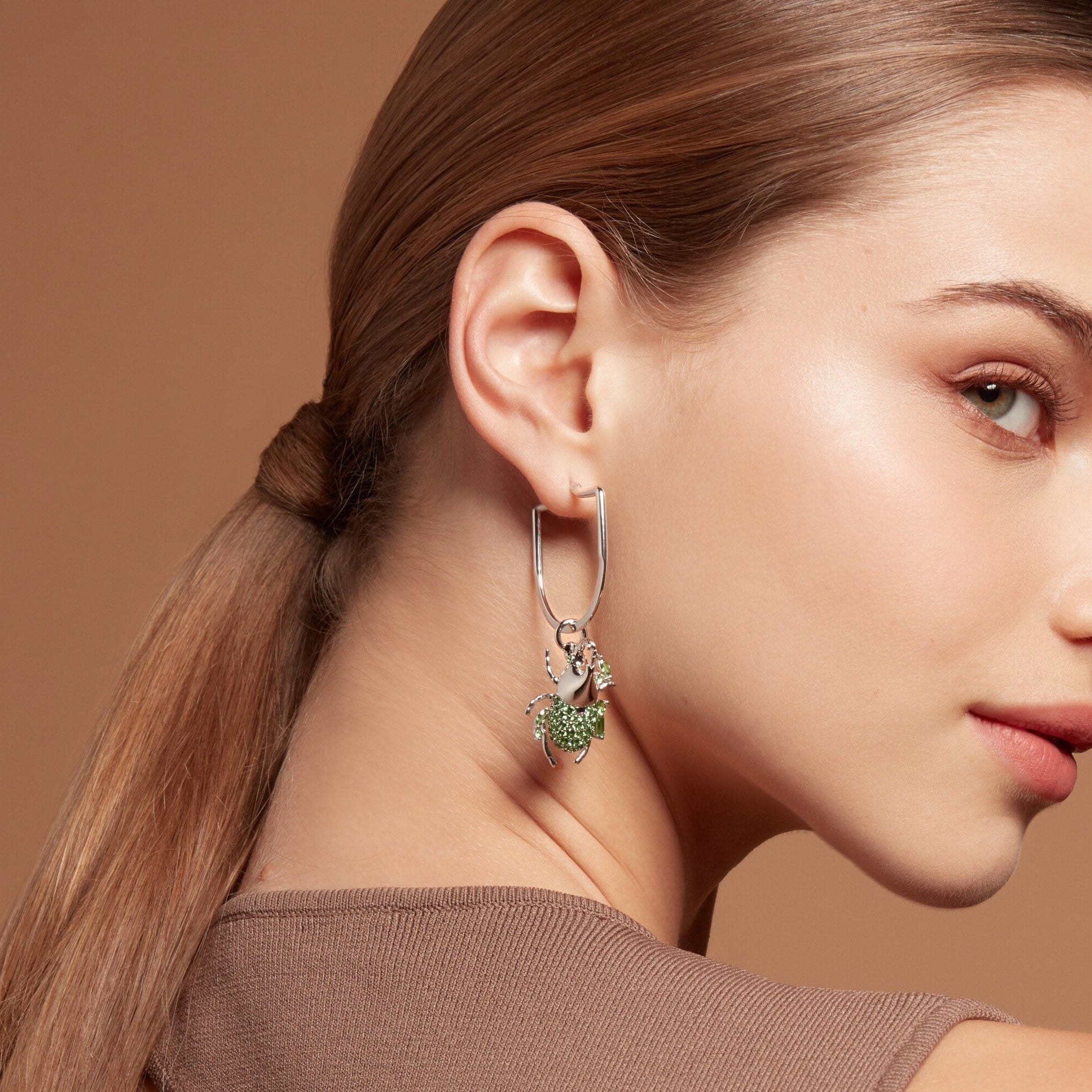 Silver hoop earring with green gemstone beetle charm on model's ear